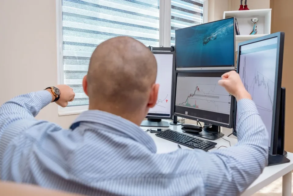 Trader observant des graphiques financiers sur plusieurs écrans dans un environnement de trading