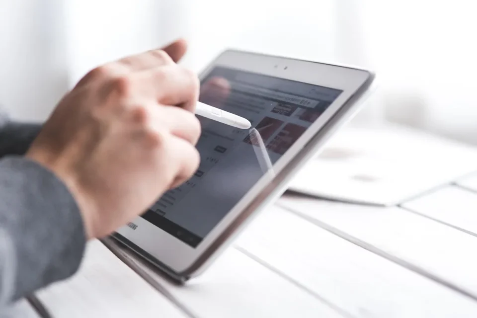 Mains anonymes tenant une tablette affichant un module de formation, documents et tasse sur un bureau