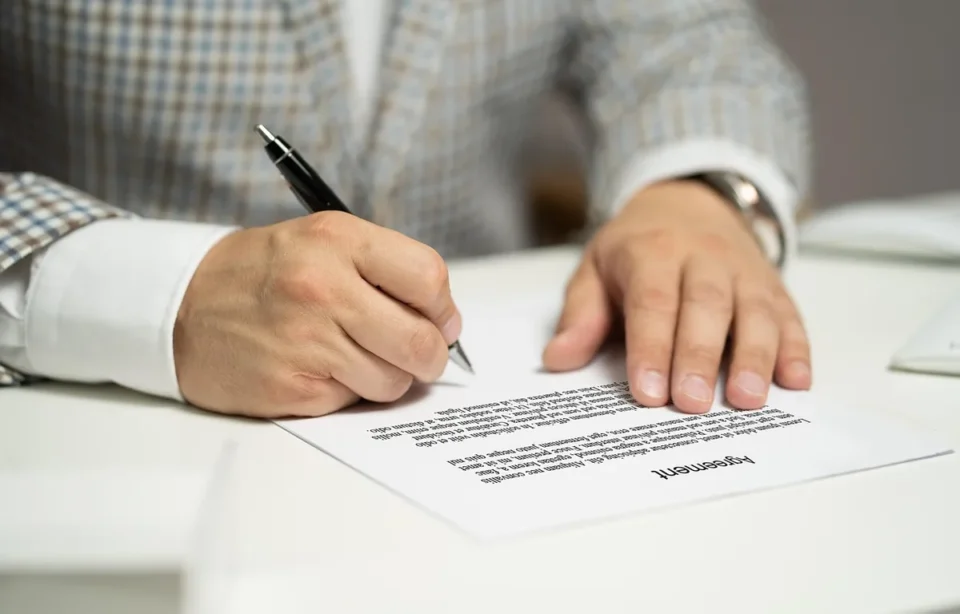 Mains signant un acte immobilier avec documents de prêt et expertise immobilière sur un bureau