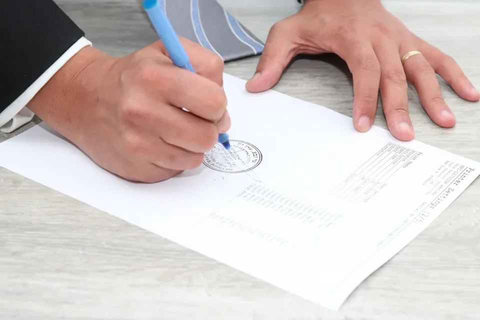 Mains anonymes signant un contrat de prêt sur un bureau, fenêtre en lumière du jour