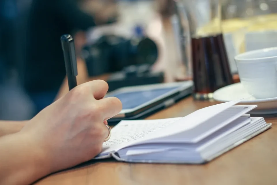 Mains d'un jeune remplissant des formulaires d'inscription sur un bureau en plein jour